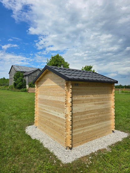 Wooden shed with a black roof in a grassy area under a blue sky with clouds.
