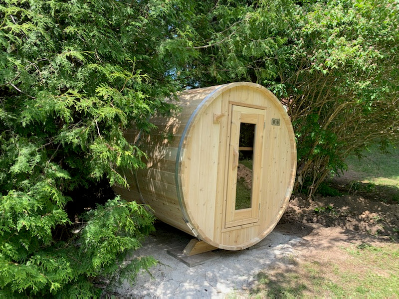 Wooden barrel-shaped sauna in a natural setting with greenery.