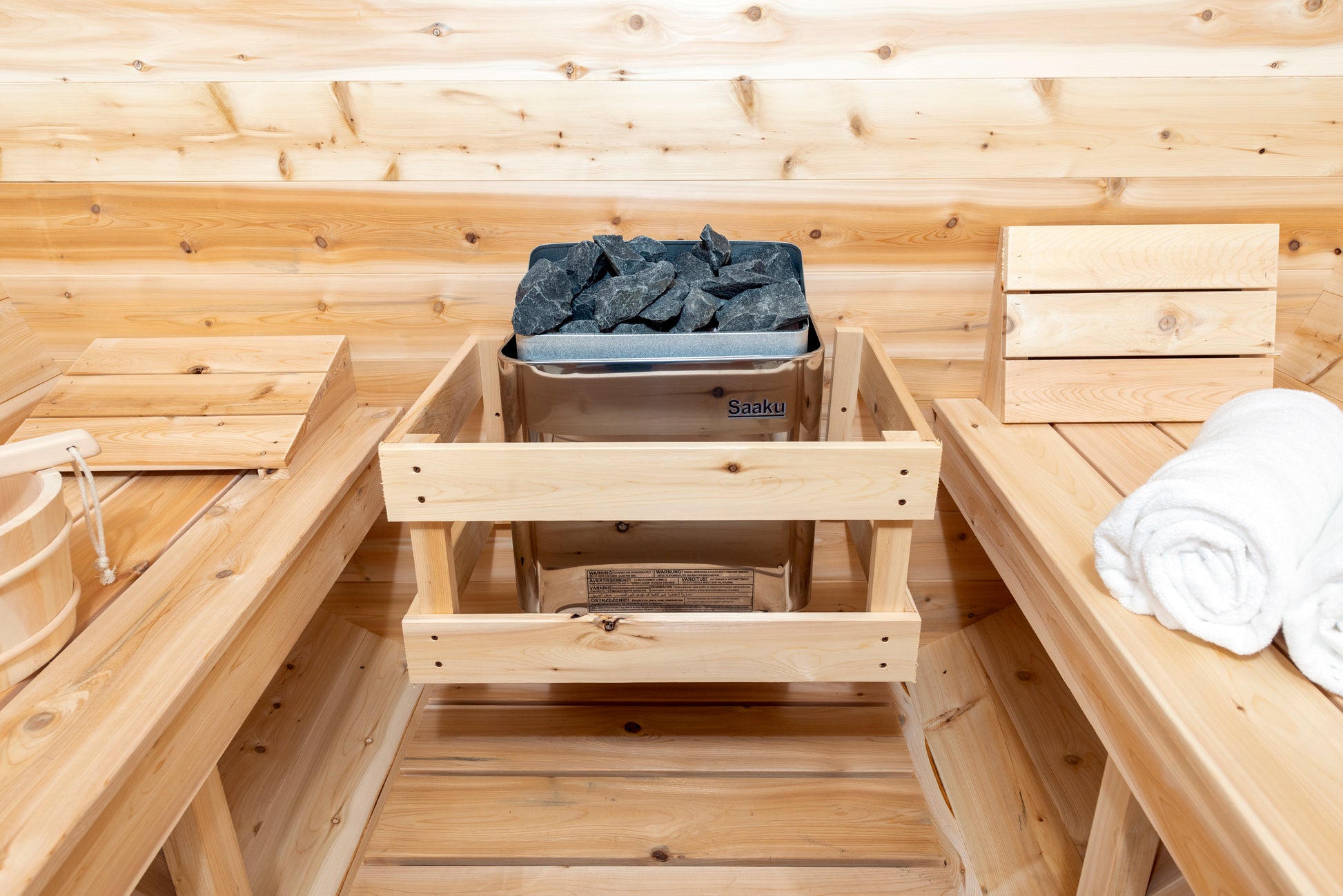 Wooden sauna interior with a bucket of rocks and folded towels.