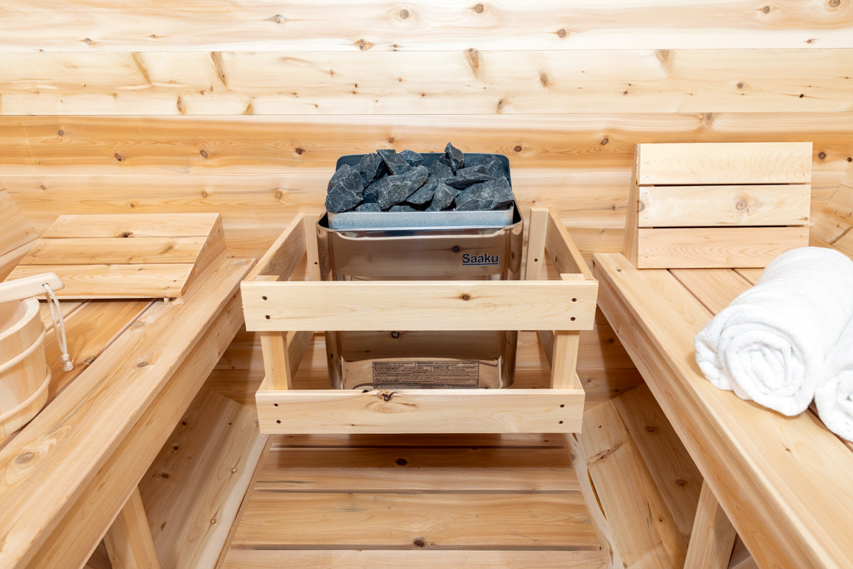 Wooden sauna interior with a bench, bucket of rocks, and towels.