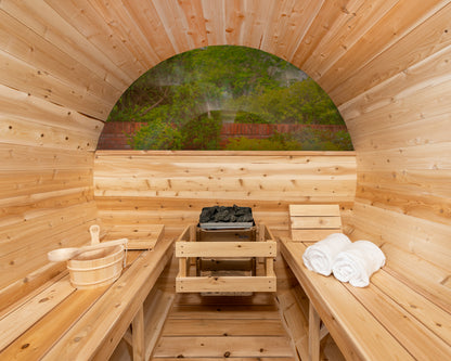 Wooden sauna interior with benches, towels, and a view of greenery outside.
