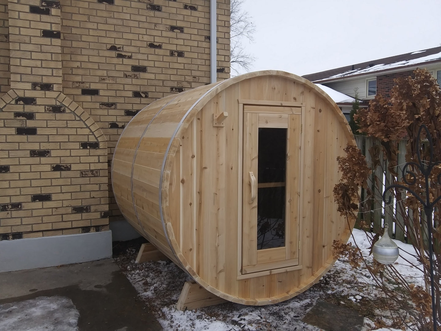 Wooden barrel shape sauna next to brick building on a snowy day